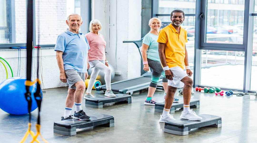 multiethnic senior athletes synchronous exercising on step platforms at gym